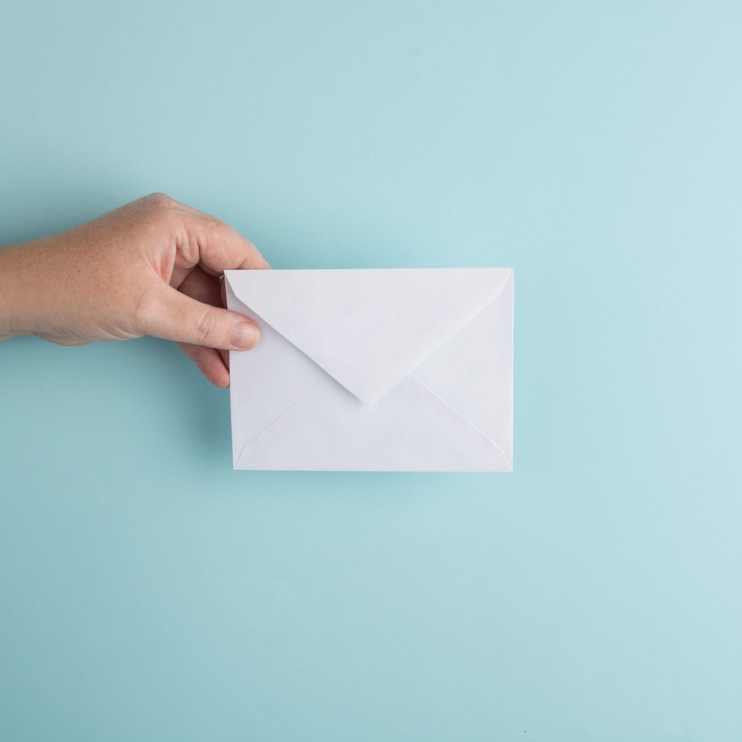 A hand holding a white custom invitation against a duck egg blue background